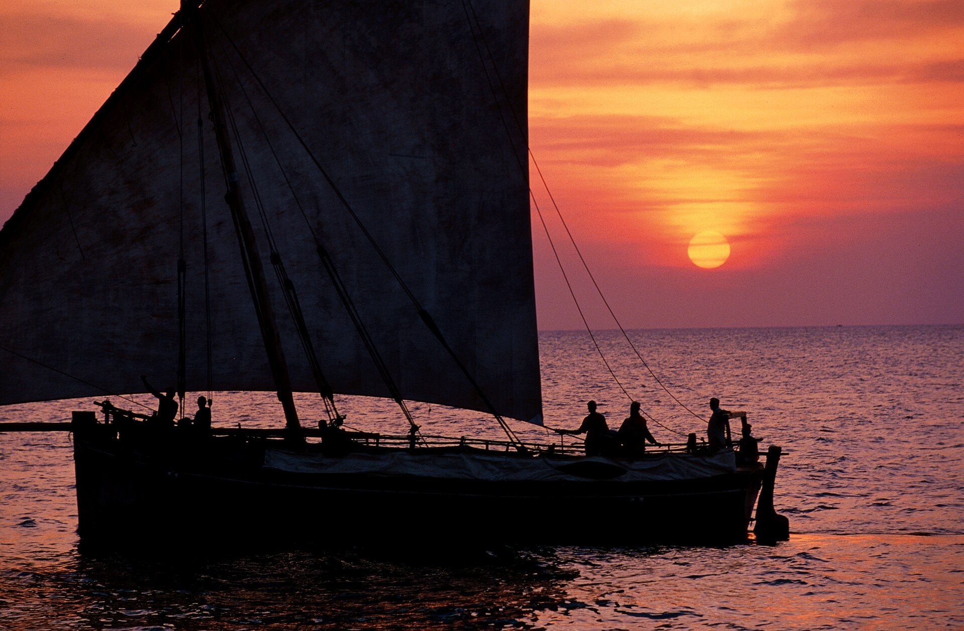 A dhow under sail against the orange sunset off Stone Town, Zanzibar